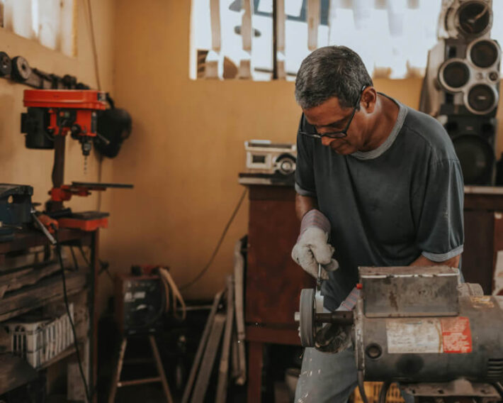 A machinist in safety glasses and gloves working in a machine shop filing a tool.