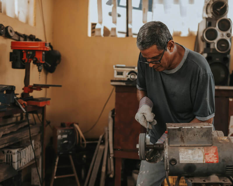 A machinist in safety glasses and gloves working in a machine shop filing a tool.
