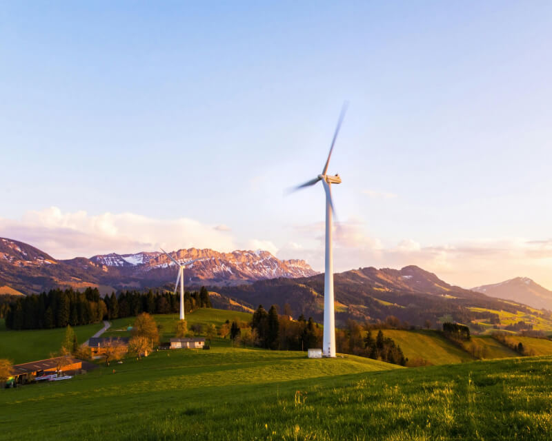 Two windmills in a field surrounded by mountains.