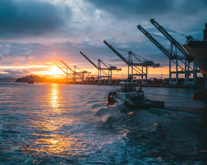 A tugboat headed out to sea surrounded by offshore drilling equipment and cranes.