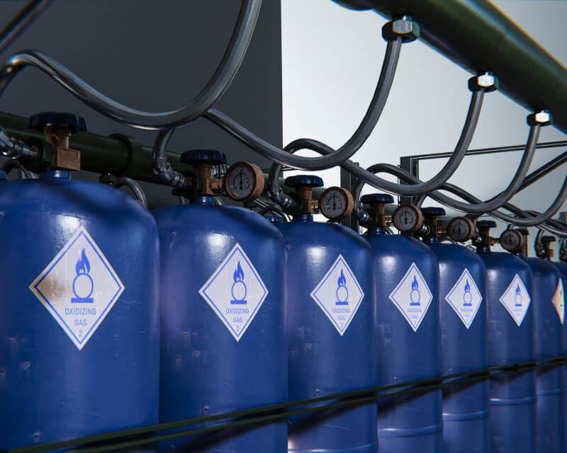 A row of gas storage cylinders connected by pipes, hoses, and valves.