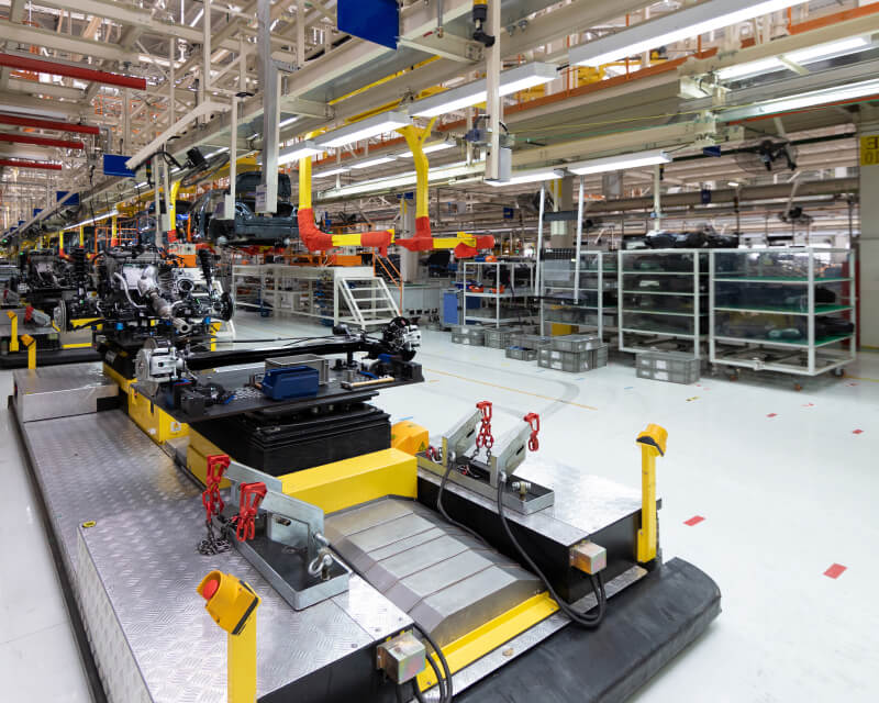 A manufacturing facility with a long line of machinery and wheeled storage carts for parts.