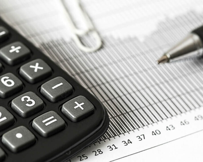 Calculator and pen poised on a paper line graph.