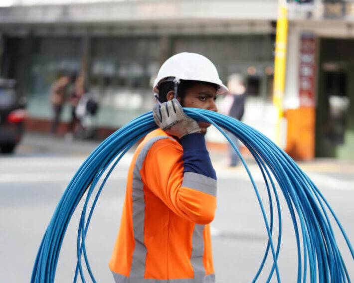 Person in safety vest and hard hat carrying blue wire on shoulder.