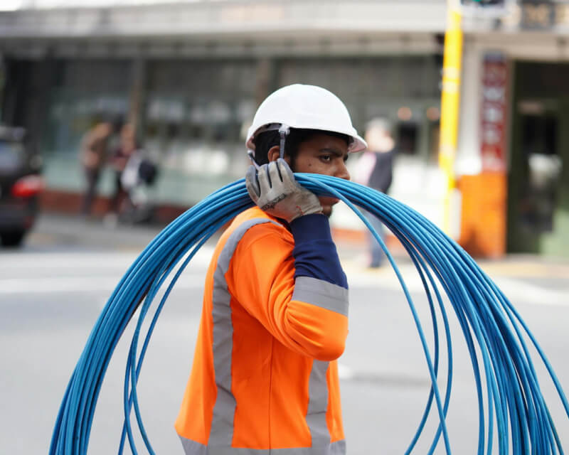 Person in safety vest and hard hat carrying blue wire on shoulder.
