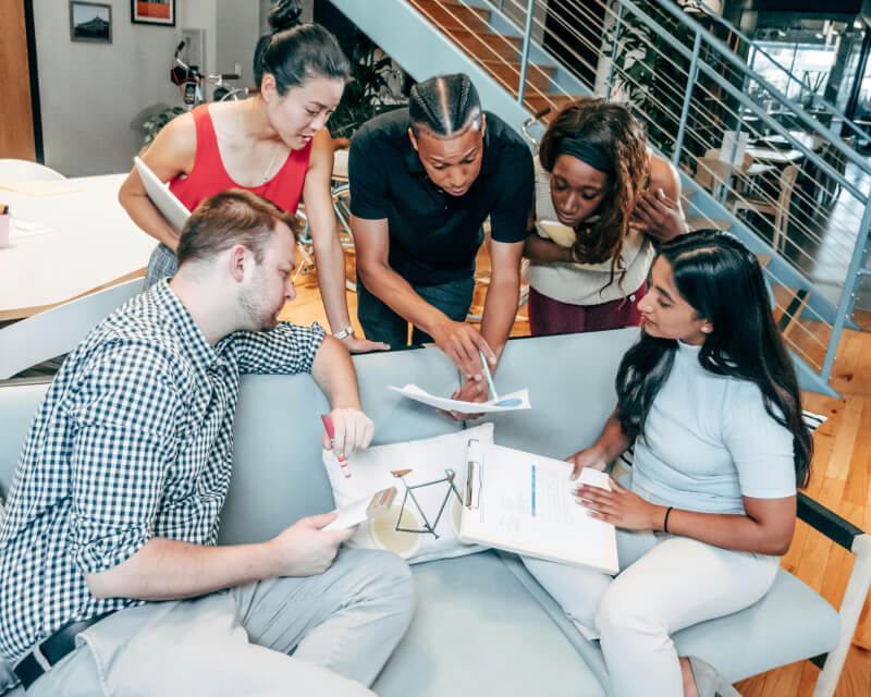 Two seated and three standing coworkers reviewing graphs on paper.