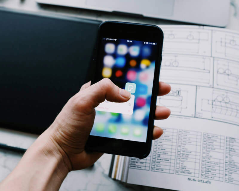 Hand holding mobile-phone downloading an app in front of computer screen.